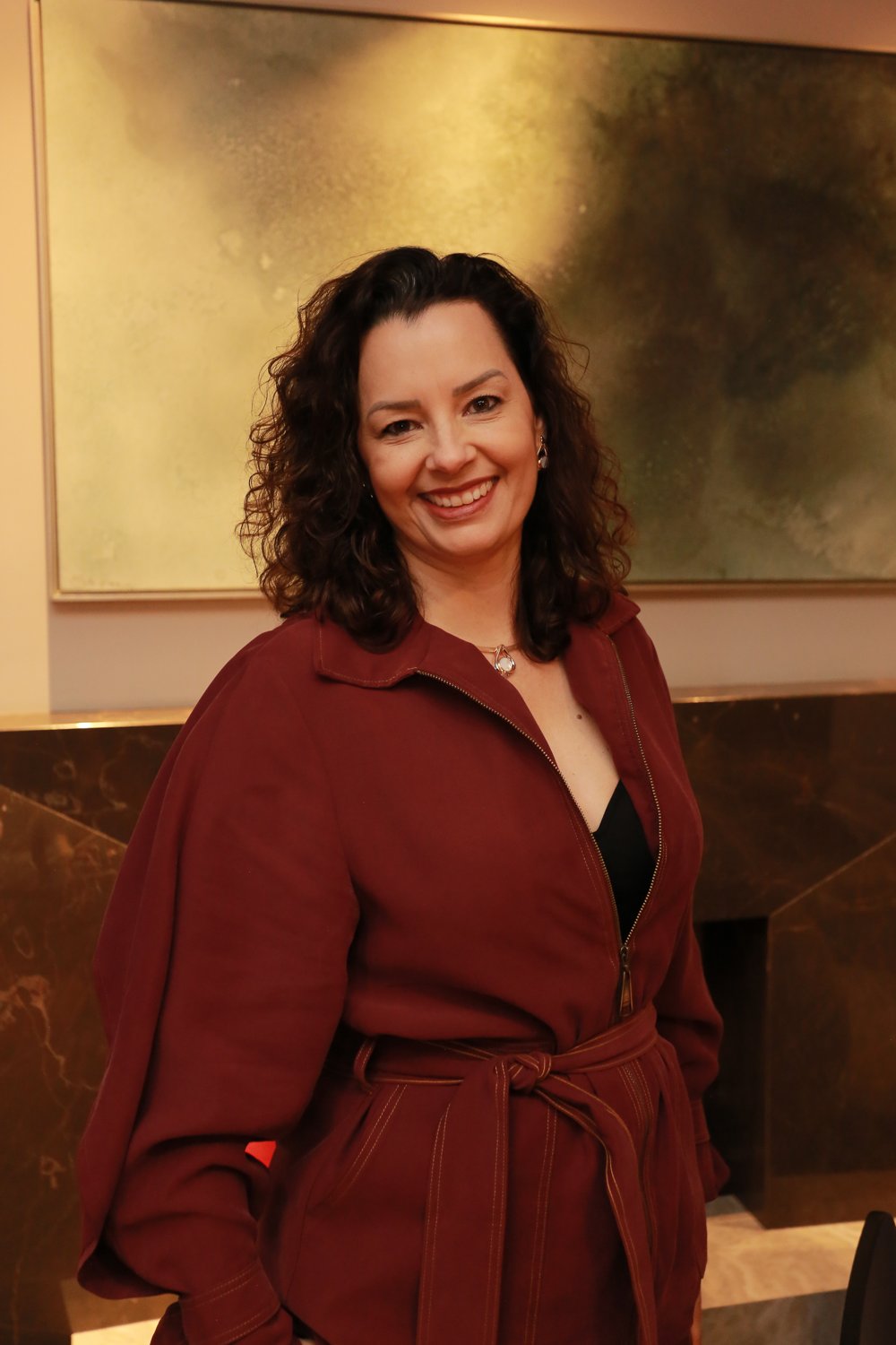 Lisa Dossi sorrindo, vestindo um trench coat bordô